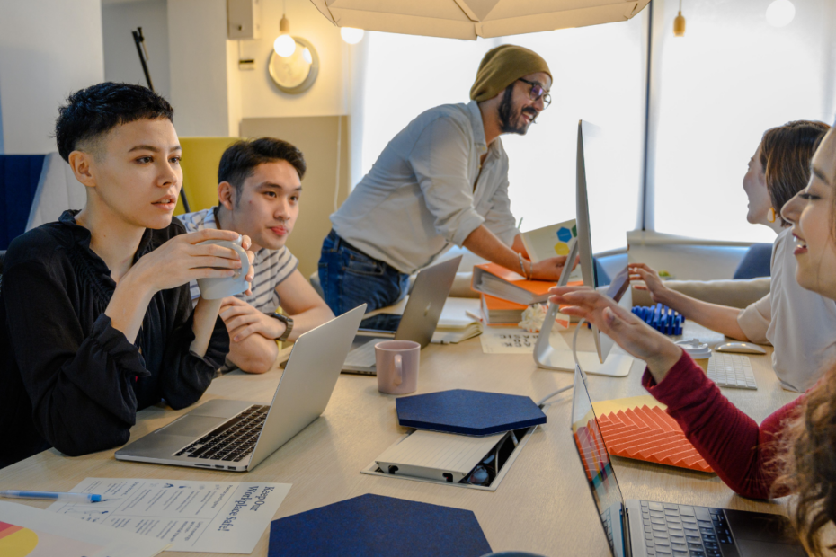 Mehrere Mitglieder eines Kreativteams sitzen gemeinsam an einem Tisch und besprechen sich in einem Meeting